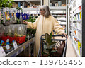 Senior woman pushing a shopping cart and selecting plants at a retail garden center 139765455
