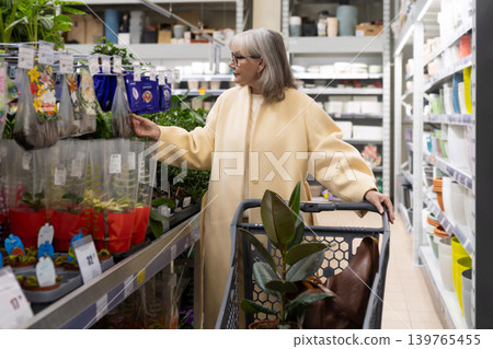 Senior woman pushing a shopping cart and selecting plants at a retail garden center Senior woman pushing a shopping cart and selecting plants at a retail garden center 139765455