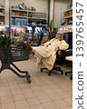 Senior woman sitting comfortably on an office chair, legs on a shopping cart in a retail store 139765457