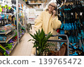 Senior woman talking on smartphone, smiling while shopping for plants and gardening tools 139765472