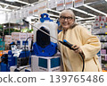 Senior woman at hardware store choosing a battery powered garden sprayer 139765486