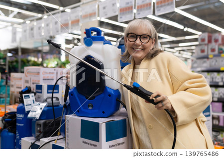 Senior woman at hardware store choosing a battery powered garden sprayer Senior woman at hardware store choosing a battery powered garden sprayer 139765486