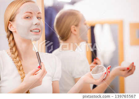 Woman applying with brush clay mud mask to her face Woman applying with brush clay mud mask to her face 139765567