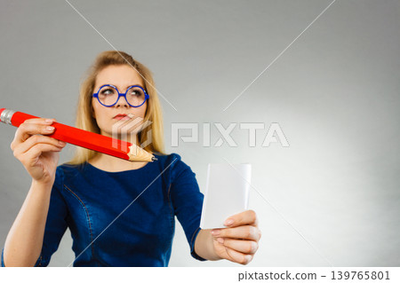 Serious woman holds big pencil note paper in hand Serious woman holds big pencil note paper in hand 139765801