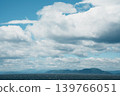 A vast natural landscape of large white clouds stretching across a blue sky and the open ocean. 139766051