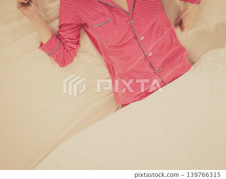 Woman lying on bed wearing pink pajamas Woman lying on bed wearing pink pajamas 139766315