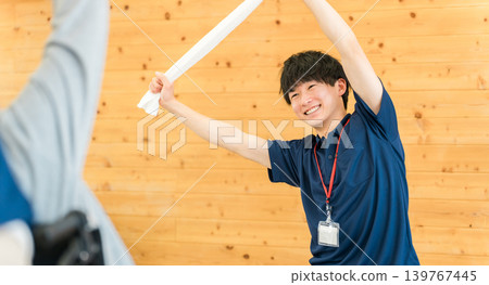 在養老院/日託中心裡,一群老年男女和一名男性工作人員正在做運動和伸展運動。 在養老院/日託中心裡,一群老年男女和一名男性工作人員正在做運動和伸展運動。 139767445