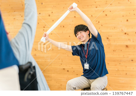 Senior men and women doing exercises and stretches at a nursing home/daycare center, along with a male staff member. Senior men and women doing exercises and stretches at a nursing home/daycare center, along with a male staff member. 139767447