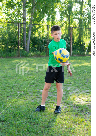 Young boy playing with a ball outdoors on a grassy field. He's wearing a green shirt and black shorts. Young boy playing with a ball outdoors on a grassy field. He's wearing a green shirt and black shorts. 139767526