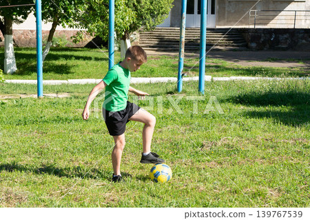 Young boy skillfully juggling a soccer ball on a grassy field. 139767539