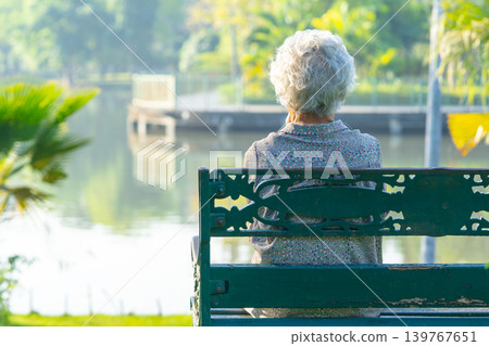 Asian elderly woman depressed and sad sitting back on bench in autumn park. 139767651