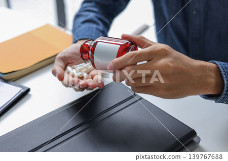 Businessman at office desk pouring medicine from bottles into his hand. Businessman at office desk pouring medicine from bottles into his hand. 139767688