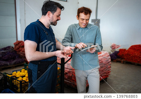Employees collaborating on digital tablet in fresh produce warehouse 139768803