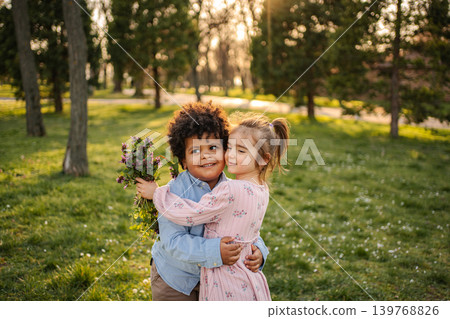 Diverse children hugging outdoors while holding wildflowers in a park Diverse children hugging outdoors while holding wildflowers in a park 139768826