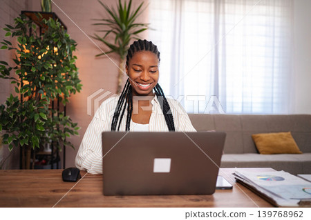 Smiling young black woman working remotely on laptop at home Smiling young black woman working remotely on laptop at home 139768962