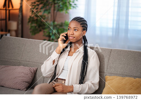 Young black woman talking on smartphone at home Young black woman talking on smartphone at home 139768972