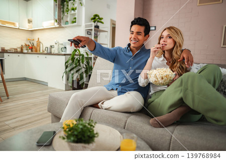Couple relaxing on sofa watching TV eating popcorn Couple relaxing on sofa watching TV eating popcorn 139768984