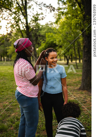 Mother styling daughter's hair outdoors in park Mother styling daughter's hair outdoors in park 139768999