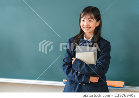 小學、國中和高中的女生穿著校服，手捧課本站在教室的黑板前 139769402