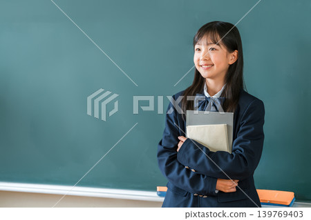 小學、國中和高中的女生穿著校服，手捧課本站在教室的黑板前 139769403