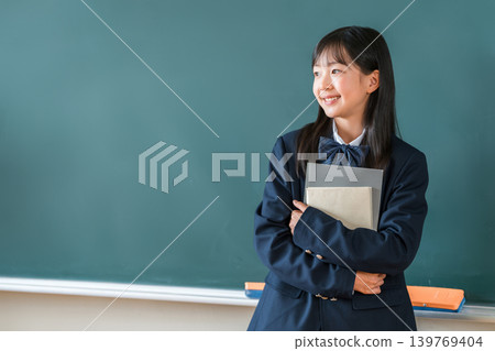小學、國中和高中的女生穿著校服，手捧課本站在教室的黑板前 139769404