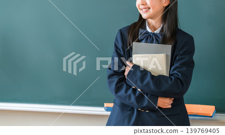 小學、國中和高中的女生穿著校服，手捧課本站在教室的黑板前 139769405