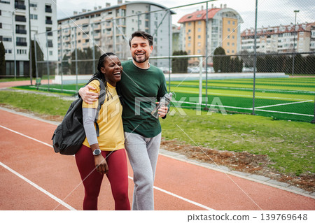 Diverse couple laughing hugging walking track after workout Diverse couple laughing hugging walking track after workout 139769648