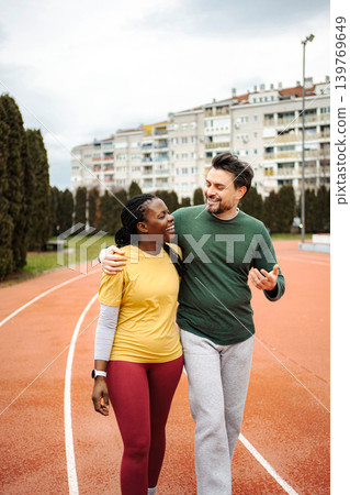 Interracial couple exercising outdoors walking on running track Interracial couple exercising outdoors walking on running track 139769649