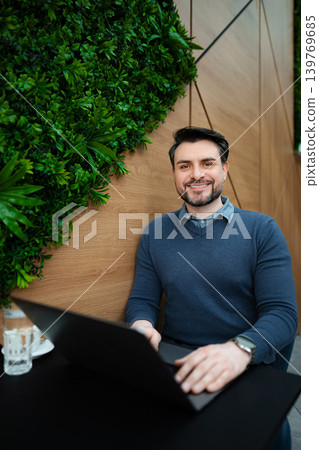 Young adult man smiling working on laptop in modern cafe 139769685