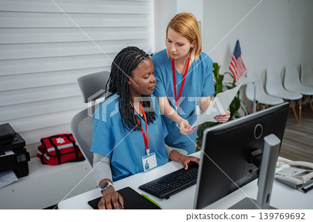 Two nurses collaborating on computer and paperwork at medical office Two nurses collaborating on computer and paperwork at medical office 139769692