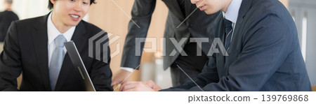 A faceless banner showing a business team of young and mid-career employees and their superiors gathered around a laptop for a meeting. 139769868