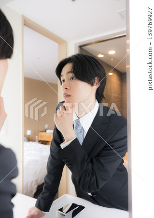 A businessman checking his appearance in a hotel mirror in the morning – an image of a pre-job interview or business trip check. First impressions are important. A businessman checking his appearance in a hotel mirror in the morning – an image of a pre-job interview or business trip check. First impressions are important. 139769927