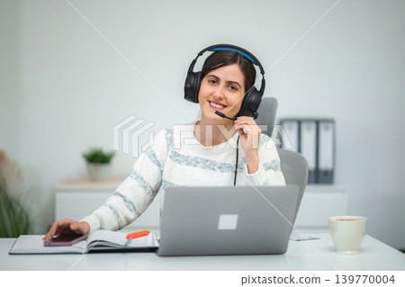 Woman wearing headset working remotely in home office Woman wearing headset working remotely in home office 139770004