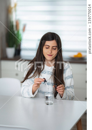 Woman taking natural medicine drops into glass of water Woman taking natural medicine drops into glass of water 139770014
