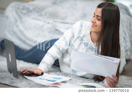 Woman freelancer working from home on laptop with documents Woman freelancer working from home on laptop with documents 139770018