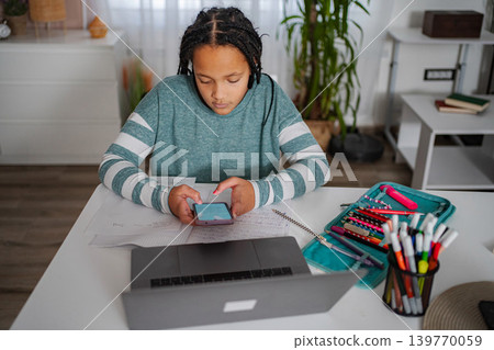Student distracted by smartphone while doing homework Student distracted by smartphone while doing homework 139770059