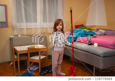 Young girl holding broom and mop cleaning messy bedroom 139770089