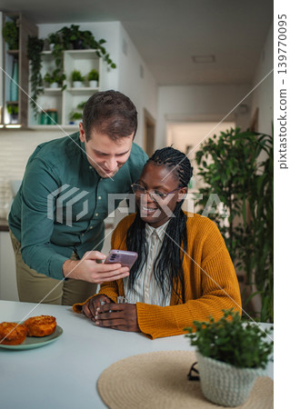 Diverse couple sharing smartphone content and laughing together Diverse couple sharing smartphone content and laughing together 139770095