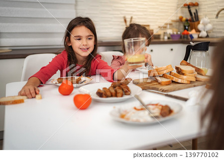 Happy girls having breakfast in kitchen with juice and sausage Happy girls having breakfast in kitchen with juice and sausage 139770102