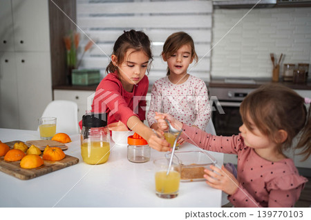 Three young girls enjoying making fresh orange juice in kitchen Three young girls enjoying making fresh orange juice in kitchen 139770103