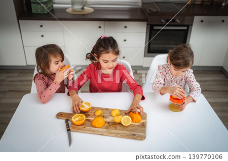 Three young girls making fresh orange juice in kitchen Three young girls making fresh orange juice in kitchen 139770106