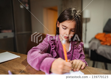 Young girl writing on paper with orange pencil Young girl writing on paper with orange pencil 139770123