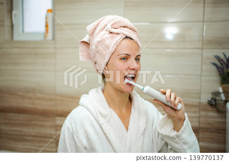 Woman brushing teeth with electric toothbrush during morning routine Woman brushing teeth with electric toothbrush during morning routine 139770137