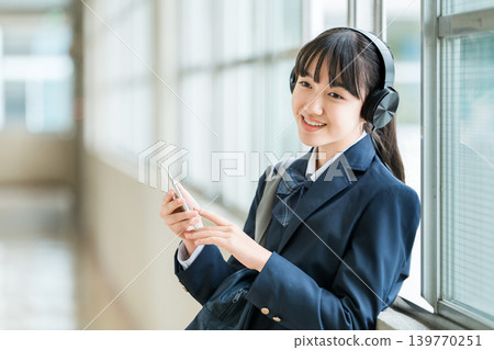 Elementary school, junior high school, and high school girls in uniforms listening to music with headphones in the school corridor Elementary school, junior high school, and high school girls in uniforms listening to music with headphones in the school corridor 139770251