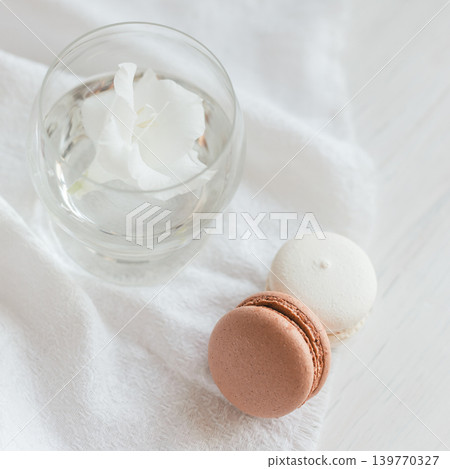 Two pastel French macarons and glass with flower on a white background. Two pastel French macarons and glass with flower on a white background. 139770327