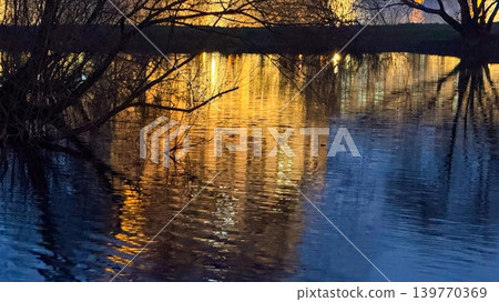 Nature Background with City Lights Reflecting in Pond Water at Night in Urban Park Nature Background with City Lights Reflecting in Pond Water at Night in Urban Park 139770369