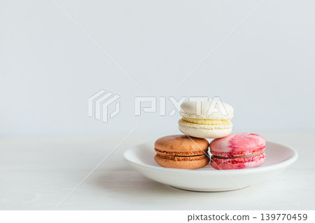Three French macarons on a white plate. Multicolored macarons. Minimal concept. Three French macarons on a white plate. Multicolored macarons. Minimal concept. 139770459