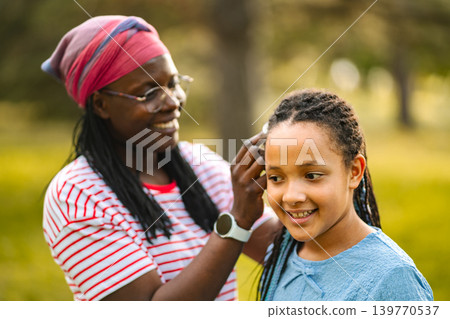 African mother bonding with daughter braiding hair outdoors African mother bonding with daughter braiding hair outdoors 139770537