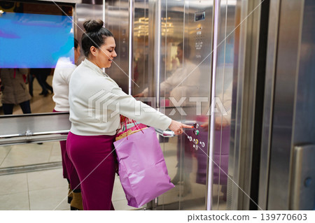 Woman with shopping bag pressing elevator button in mall Woman with shopping bag pressing elevator button in mall 139770603