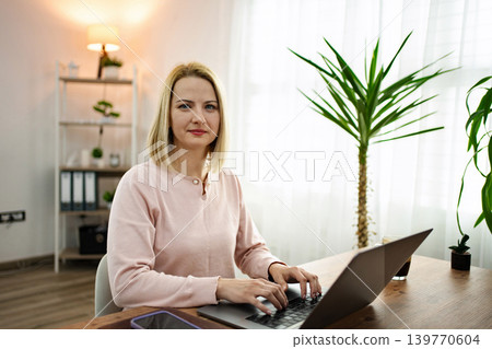 Bright workspace with a focused woman typing on a laptop surrounded by plants, creating a serene atmosphere for productivity Bright workspace with a focused woman typing on a laptop surrounded by plants, creating a serene atmosphere for productivity 139770604